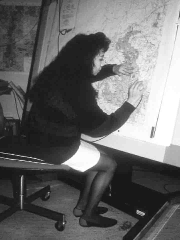 Una mujer trabajando en un centro de operaciones analizando datos sobre un gran mapa colocado en una pantalla vertical.